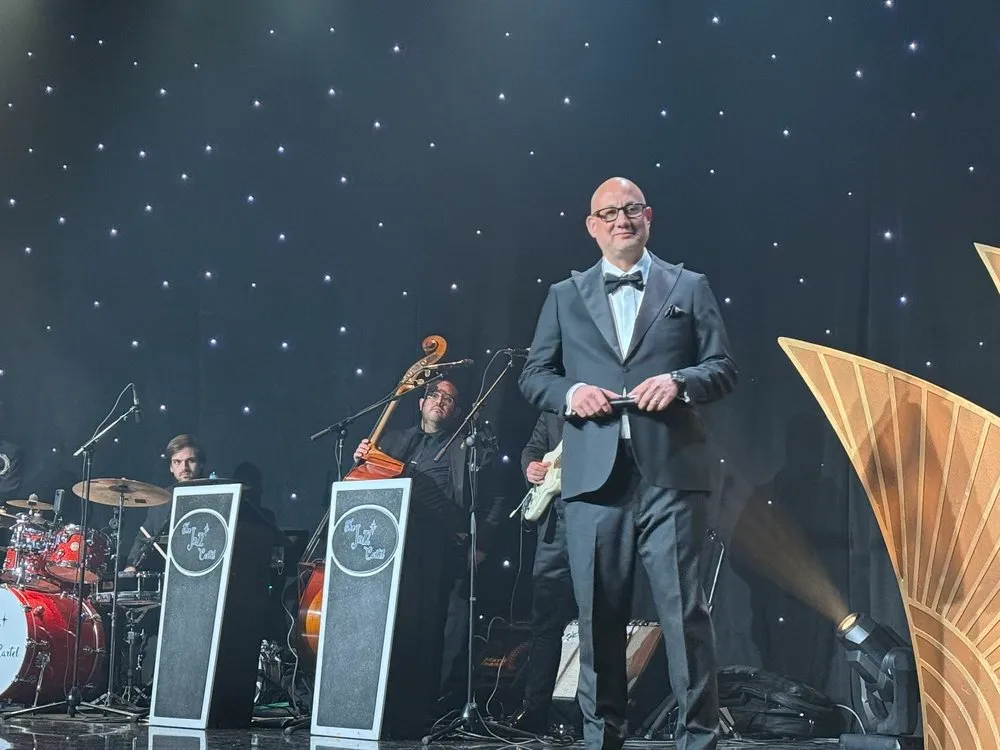 Luis Giraldo performing on stage at the Beverly Hilton, in tuxedo, warm tungsten lighting